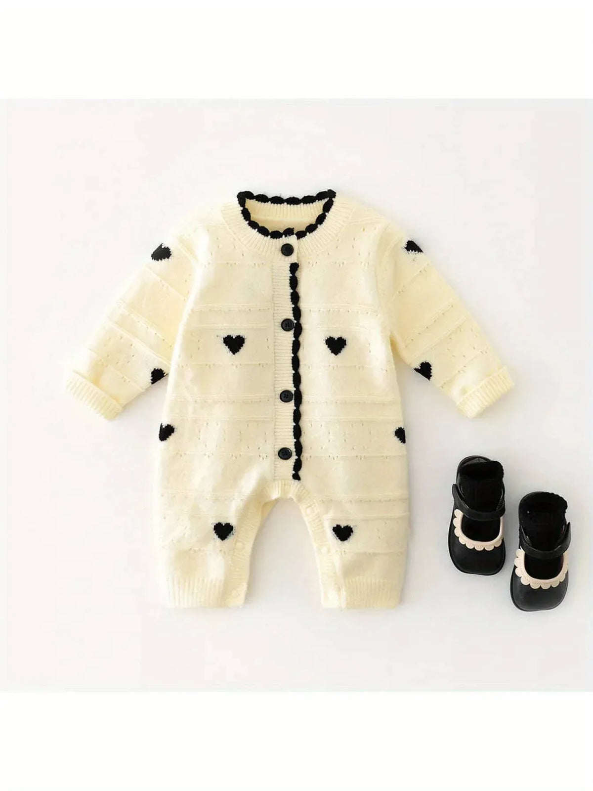 Cream knitted baby romper with hearts in black, laid flat with black baby shoes for newborns