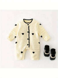 Cream knitted baby romper with hearts in black, laid flat with black baby shoes for newborns