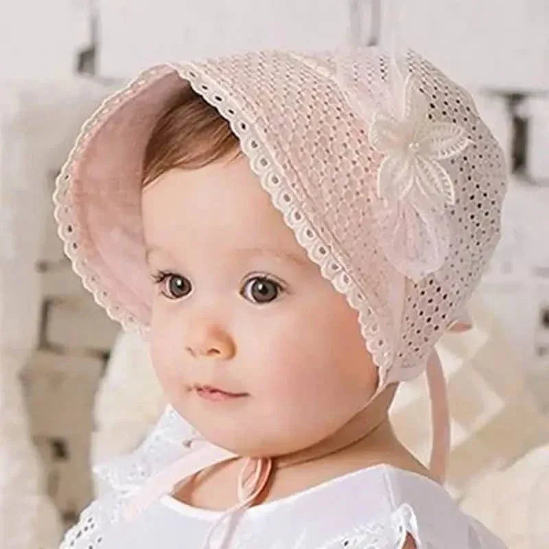 baby wearing pink lace baby bonnet with floral decoration sitting indoors