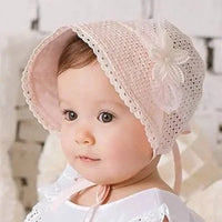 baby wearing pink lace baby bonnet with floral detail sitting indoors