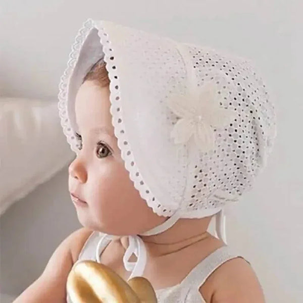 Baby wearing white lace baby bonnet with floral detail holding a golden toy