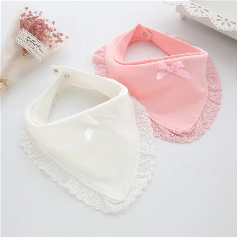 White and pink lace bib for babies with delicate bow accents on a flat surface