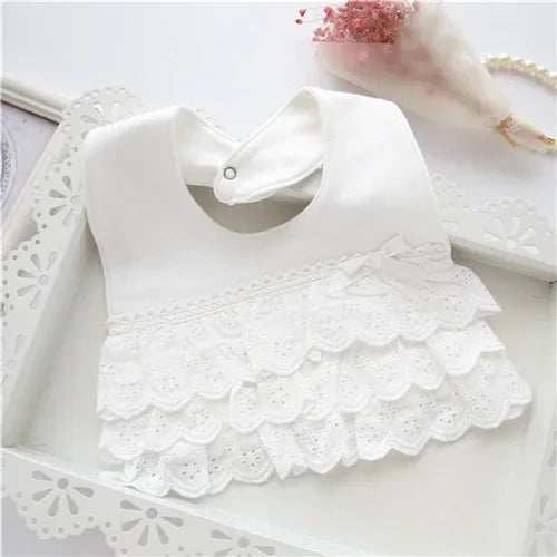 White lace bib for babies with scalloped edges and small bow detail displayed on decorative tray