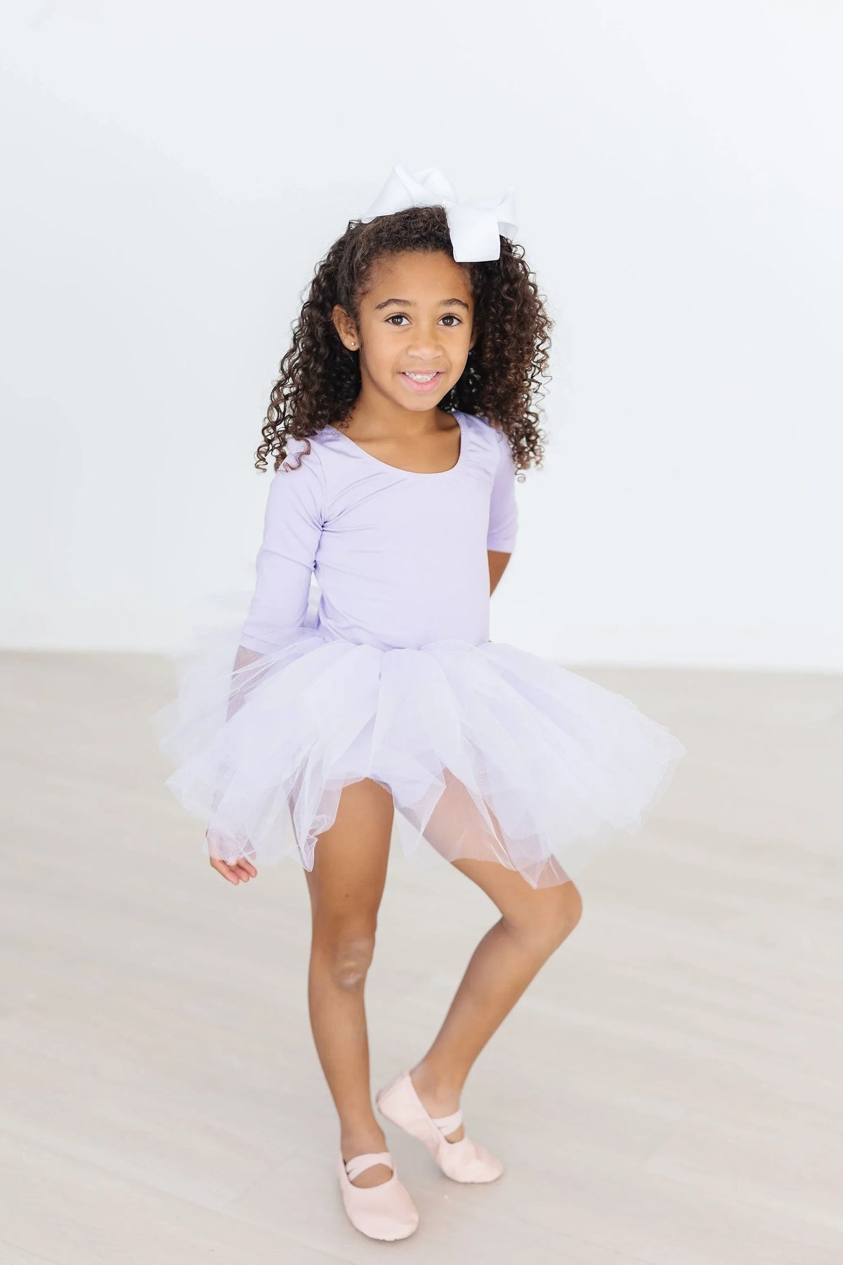 Lavender tutu leotard for toddlers with sleeves worn by young girl with white bow