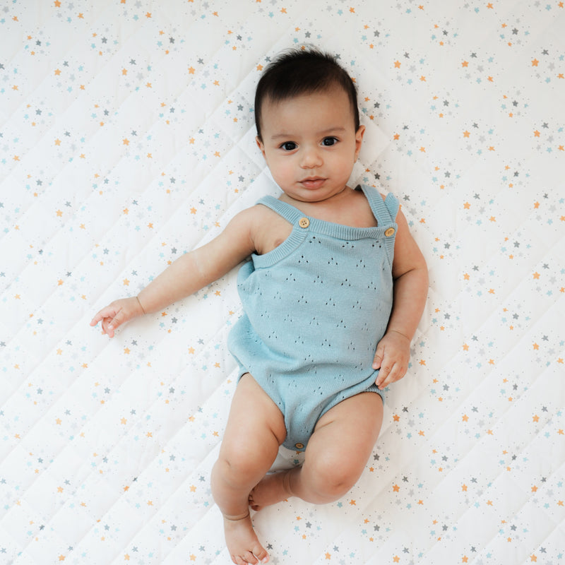 A baby lying comfortably on a Goosewaddle® Super Soft Play Mat, featuring a cozy quilted design with a celestial star pattern, highlighting the mat's plush and inviting surface for safe play and exploration.