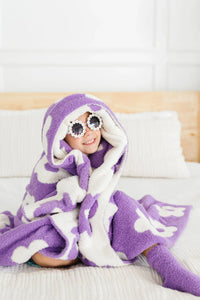 Young girl wrapped in lilac flower throw blanket for girls sitting on bed wearing sunglasses and smiling