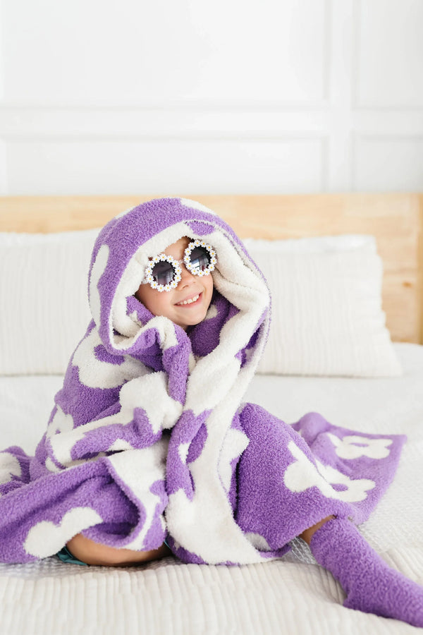 Young girl wrapped in lilac flower throw blanket for girls sitting on bed wearing sunglasses and smiling