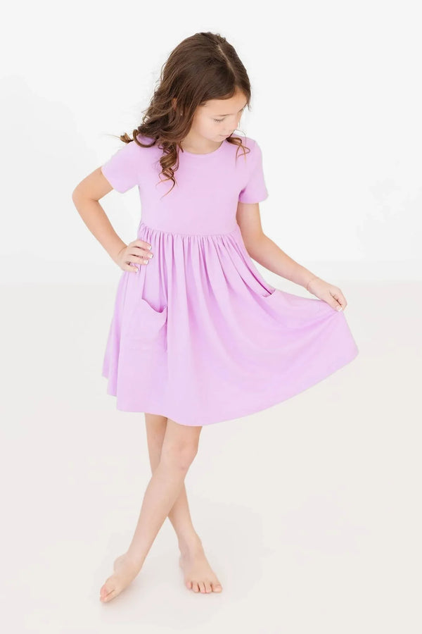Young girl wearing lilac twirl dress for girls by Mila & Rose holding the skirt while posing
