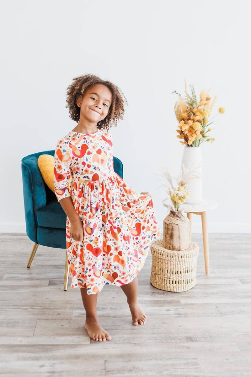 Little girl wearing a colorful little red hen girls dress with 3/4 sleeves and twirl pocket detail