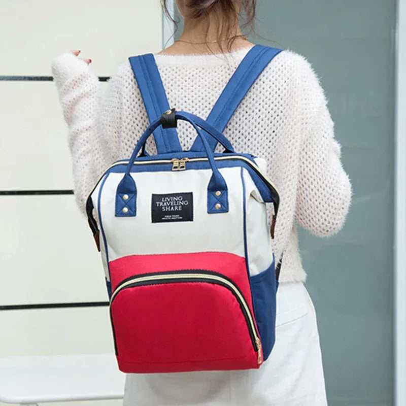 woman wearing white sweater with blue red multifunctional insulated diaper bag backpack