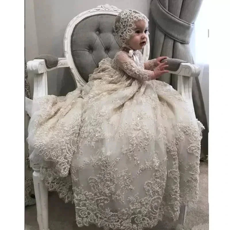 baby wearing ivory luxury lace christening gown sitting on vintage white chair reaching forward