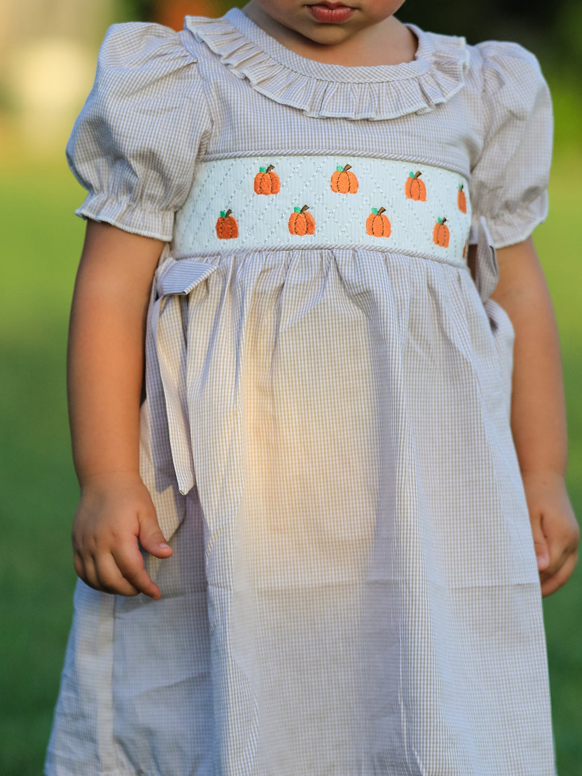Girl in plaid smock dress with orange pumpkin embroidery for fall, Halloween, and Thanksgiving.