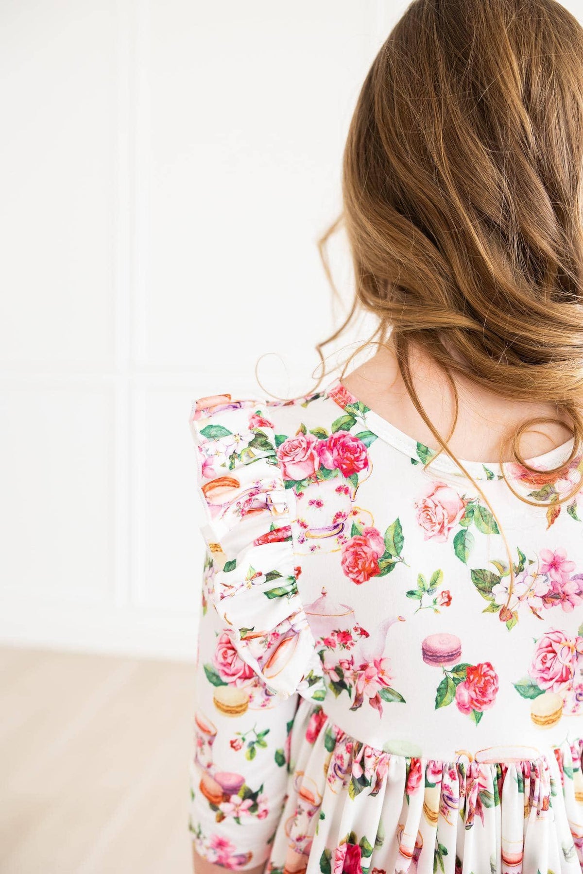 young girl wearing white floral ruffle twirl dress with pink roses and macarons print