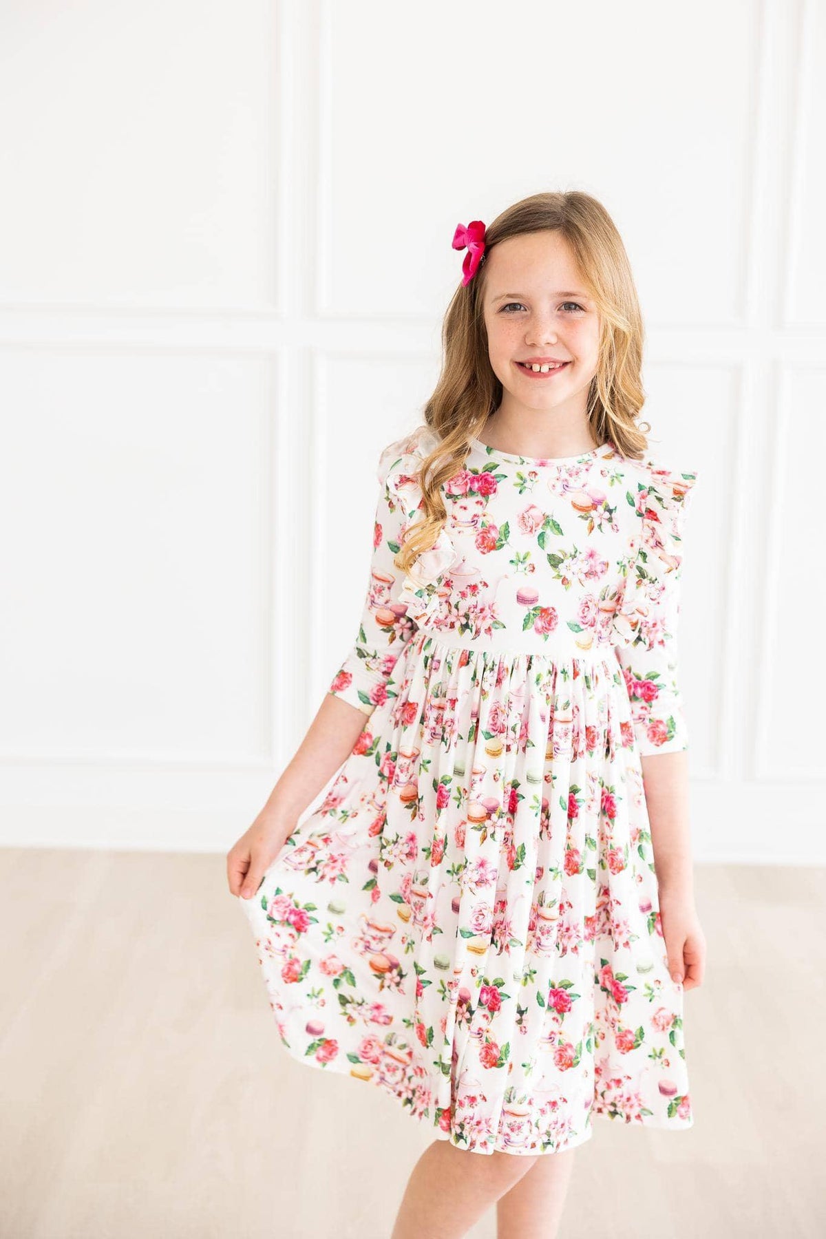 young girl wearing white floral ruffle twirl dress with 3/4 sleeves smiling and holding dress