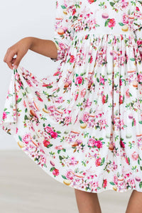 young girl wearing white floral ruffle twirl dress holding the skirt out to twirl