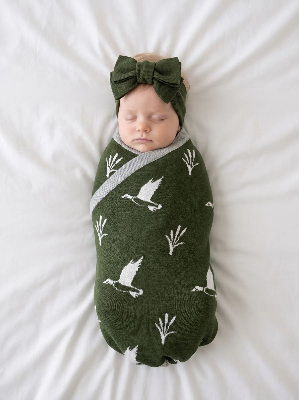 Newborn swaddled in green mallard duck jacquard knit baby blanket on white bedding