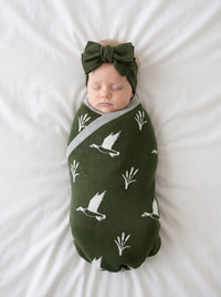 Newborn swaddled in green mallard duck jacquard knit baby blanket on white bedding