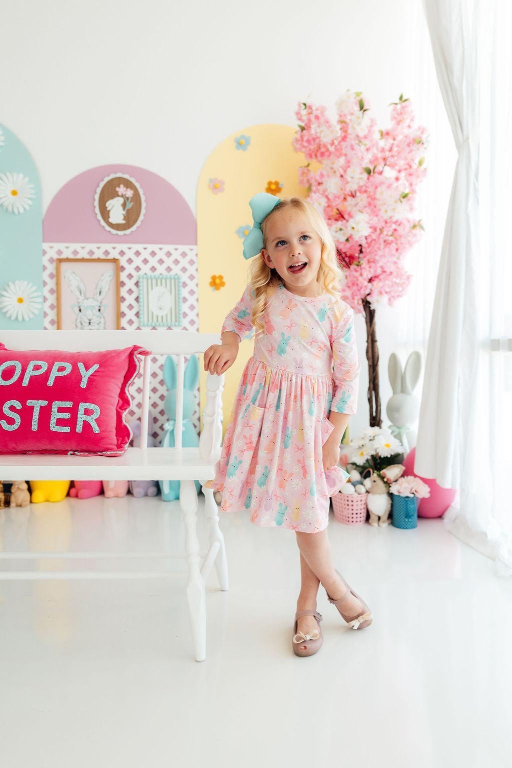 Girl in pastel pink Preppy Peeps 3/4 sleeve pocket twirl dress with bunny print and blue bow.