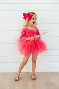 Young girl in magenta velvet long sleeve tutu leotard with matching bow, perfect for dance class or play.