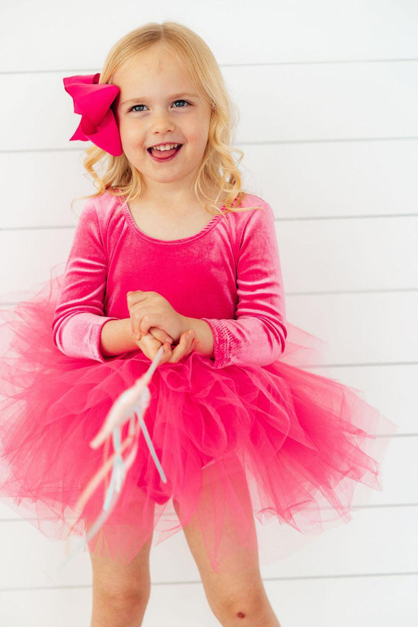 Little girl wearing a magenta velvet long sleeve leotard with a full tulle tutu skirt and matching bow. Perfect for dance or play.