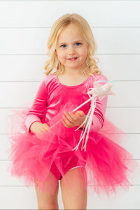 Toddler girl wearing a magenta velvet long sleeve leotard with a fluffy tulle tutu skirt, holding a star wand.