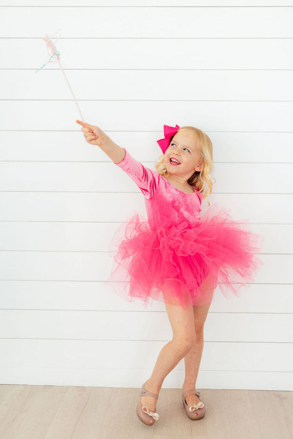 Little girl in a magenta velvet long-sleeve leotard with a fluffy multi-layer tulle tutu skirt holding a wand.