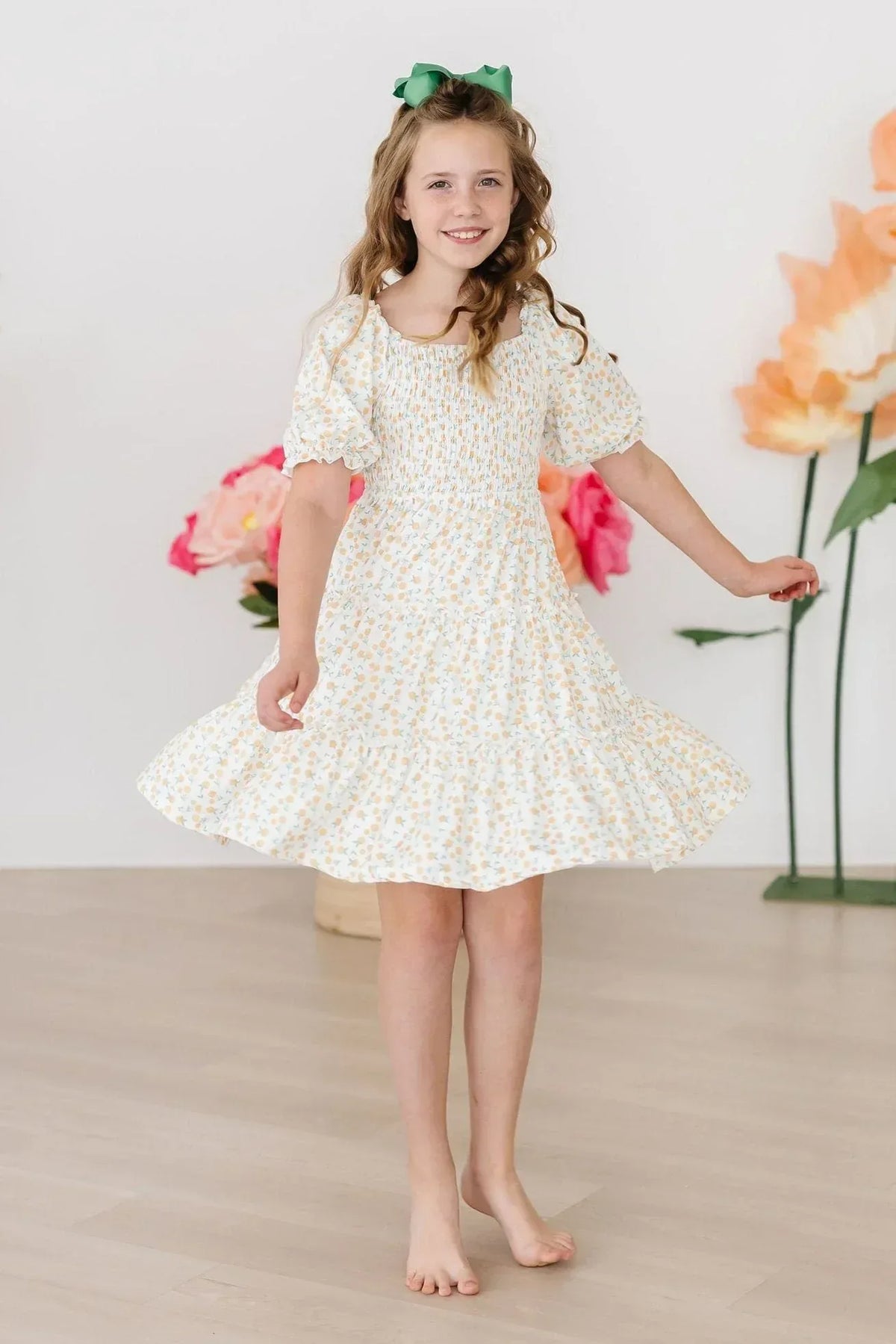 Young girl wearing marigold smocked dress twirling with a green bow in her hair