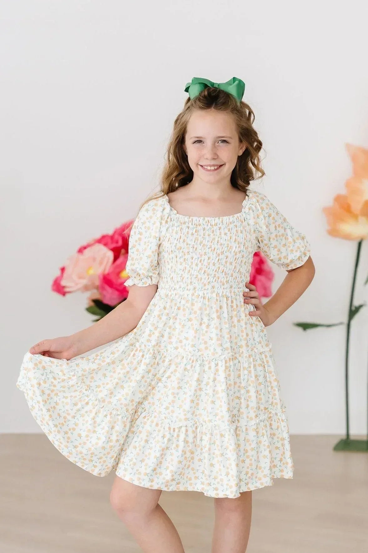 Young girl wearing marigold smocked dress with ruffles and puff sleeves smiling and holding dress