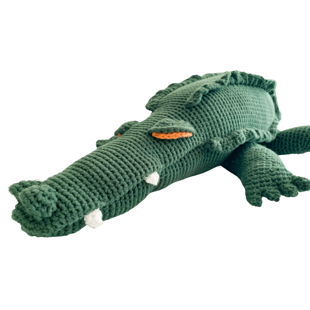 Large green crocheted crocodile stuffed animal with textured back, white teeth, and orange eye detail.