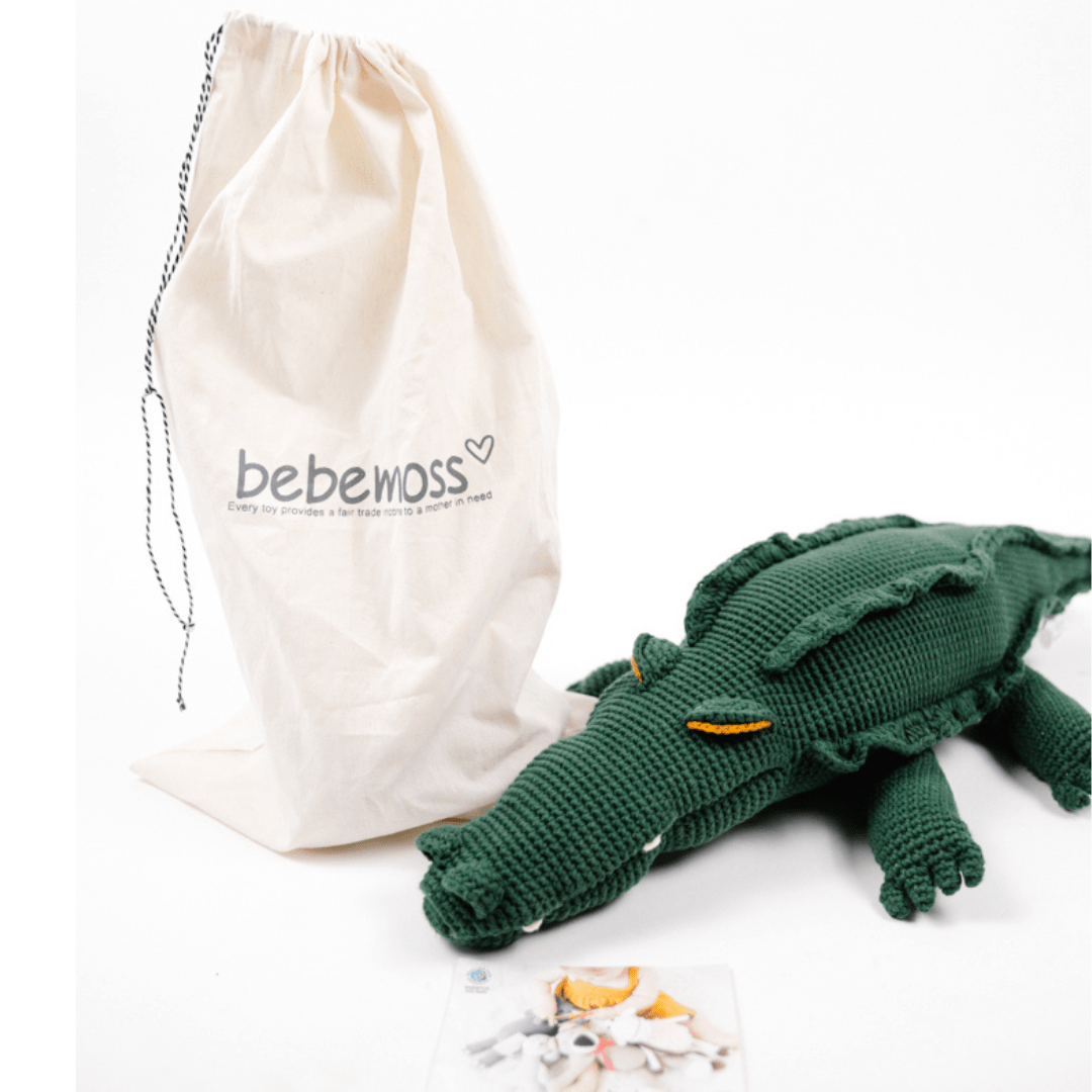 Large green crocheted crocodile with toothy face and ridged back, displayed next to a beige fabric storage bag.