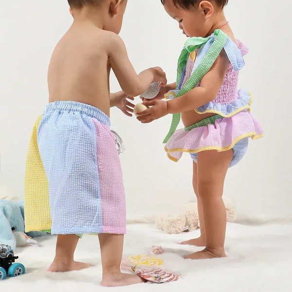 toddler boy and girl wearing pastel matching seersucker swimsuits for siblings with ruffle and tie details