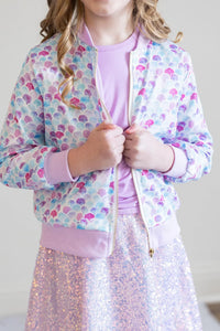 girl wearing pastel mermaid satin jacket for girls with purple seashell pattern and pink cuffs