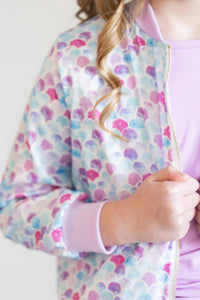 girl wearing mermaid satin jacket for girls with pastel shell pattern and pink cuffs