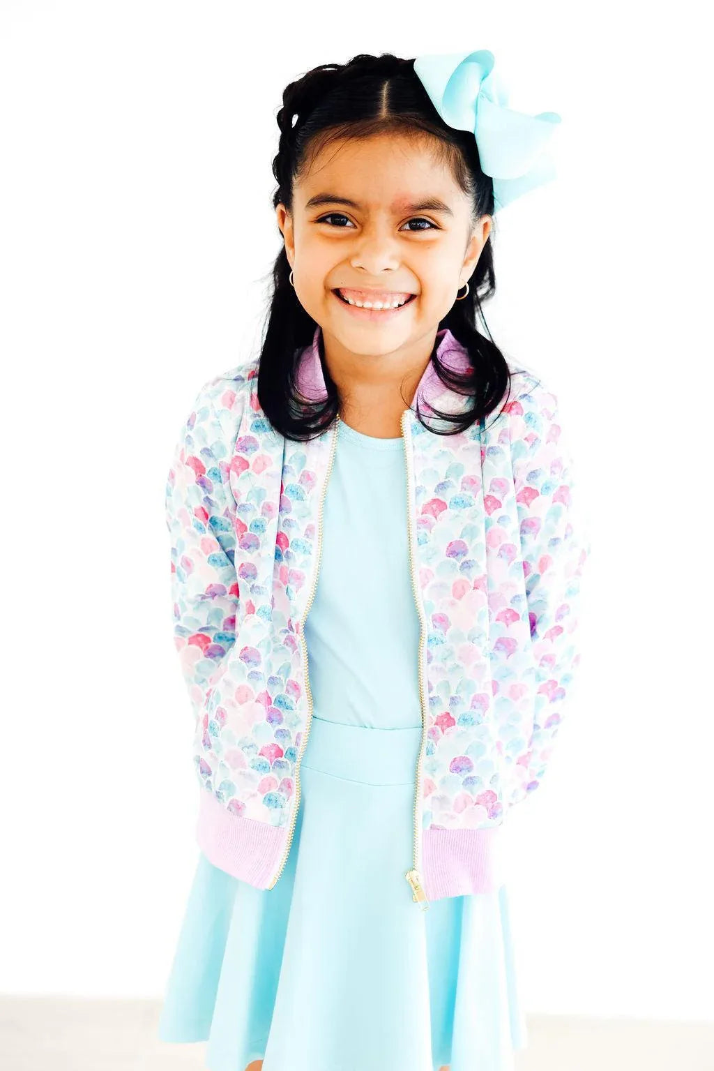 Young girl wearing pastel mermaid satin jacket for girls with seashell pattern and pink cuffs smiling
