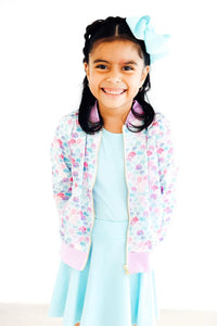 Young girl wearing pastel mermaid satin jacket for girls with seashell pattern and pink cuffs smiling