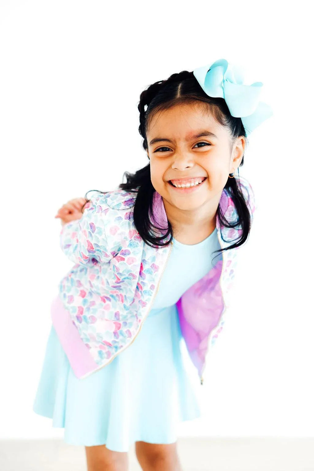 smiling young girl wearing a pastel mermaid satin jacket for girls with floral pattern and pink trim bending forward