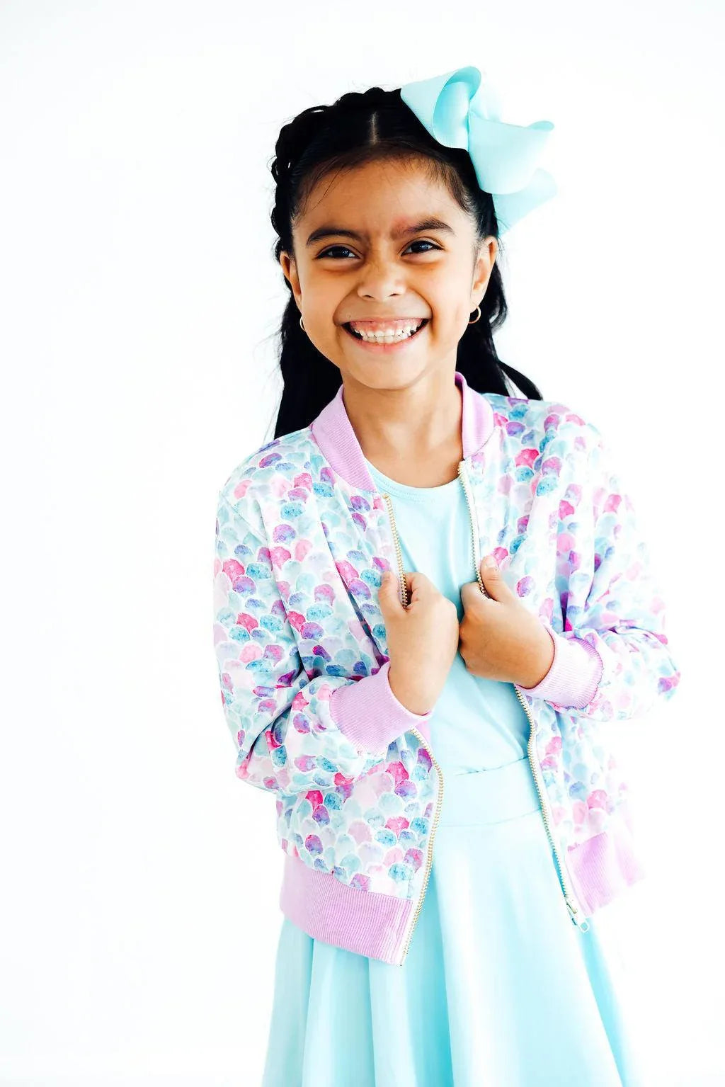 smiling young girl wearing a colorful mermaid satin jacket for girls over a light blue dress