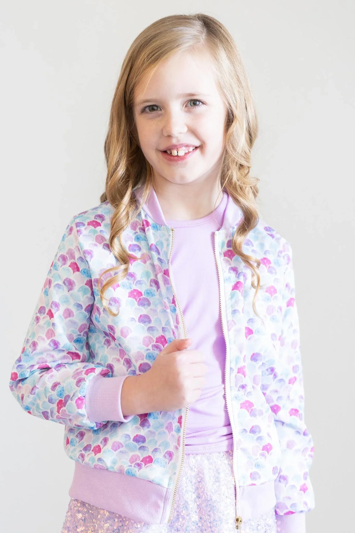 young girl wearing pastel mermaid satin jacket for girls with shell pattern standing and smiling