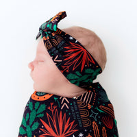 The SoftKnot Bow Desert Cactus (Midnight) baby head-wrap on navy fabric with cactus print.