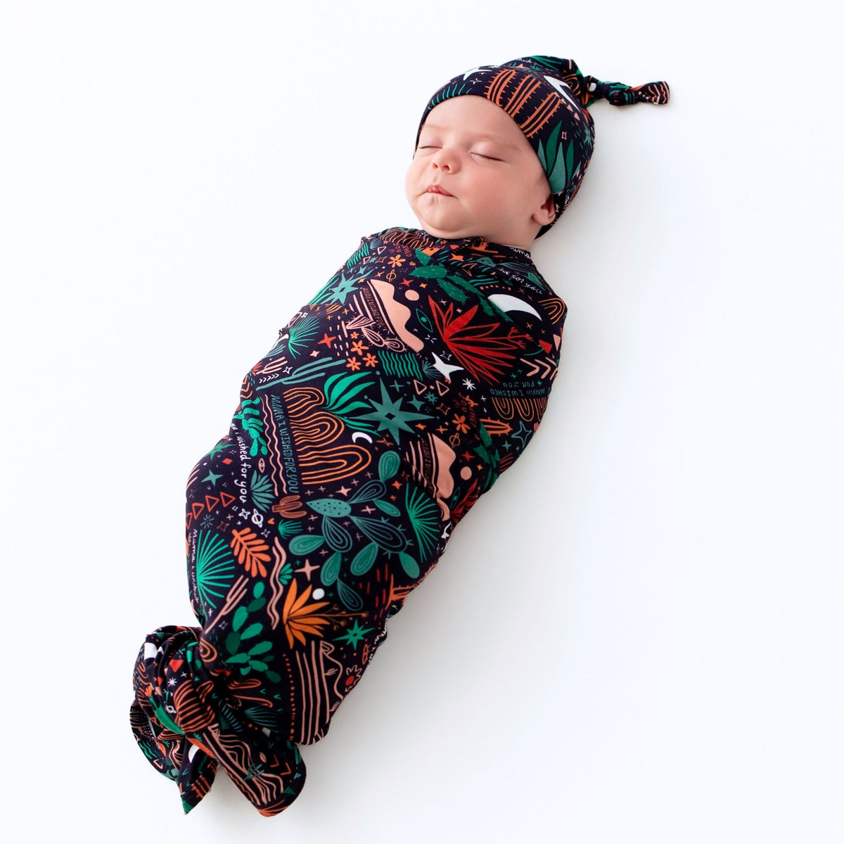 Newborn sleeping while swaddled in Desert Cactus Midnight Forever Swaddle Blanket with matching hat.