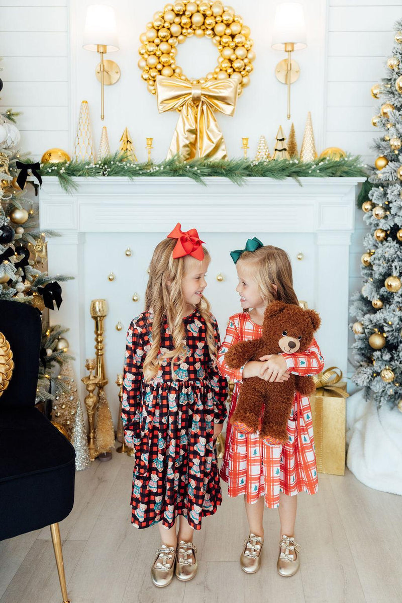 Two girls dressed in the Plaid Trees Long Sleeve Pocket Girls Twirl Dress, joyfully interacting in a festive setting decorated with holiday ornaments and a lavish wreath, ideal for Christmas celebrations.