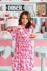 Girl wearing Vintage Cakes Long Sleeve Pocket Twirl Dress, holding a pink cake in a retro diner.