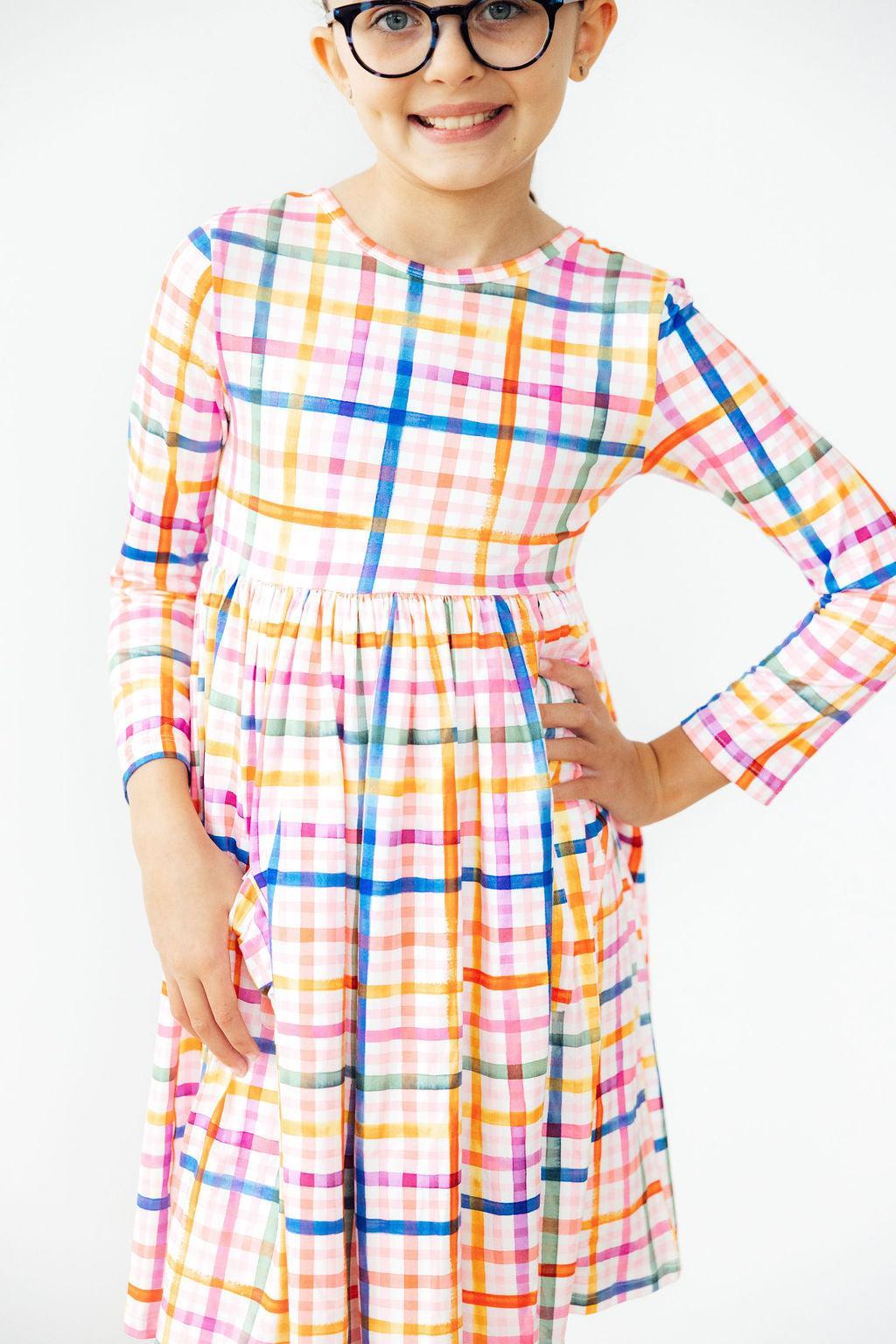 Stylish girl in Plaid About You L/S Pocket Twirl Dress poses with confidence, showcasing the colorful plaid design and playful twirl skirt.