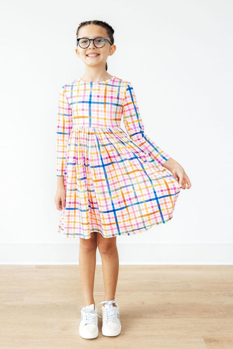 Bright and cheerful Plaid About You Long Sleeve Pocket Twirl Dress showcased by a smiling girl, perfect for twirling and playtime adventures.