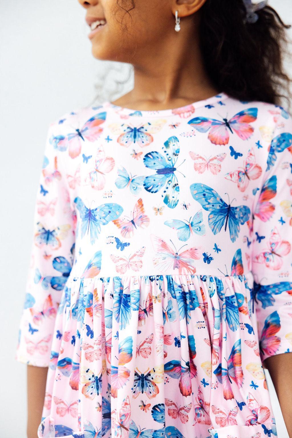 Little Flutters 3/4 Sleeve Pocket Twirl Dress featuring vibrant butterfly patterns on a young girl smiling, showcasing the joyful design and twirl-friendly skirt.