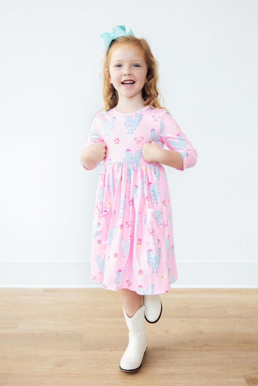 Little Miss Chickie 3/4 Sleeve Pocket Twirl Dress worn by a smiling young girl in a bright and fun pose, showcasing the full-circle skirt and playful design.