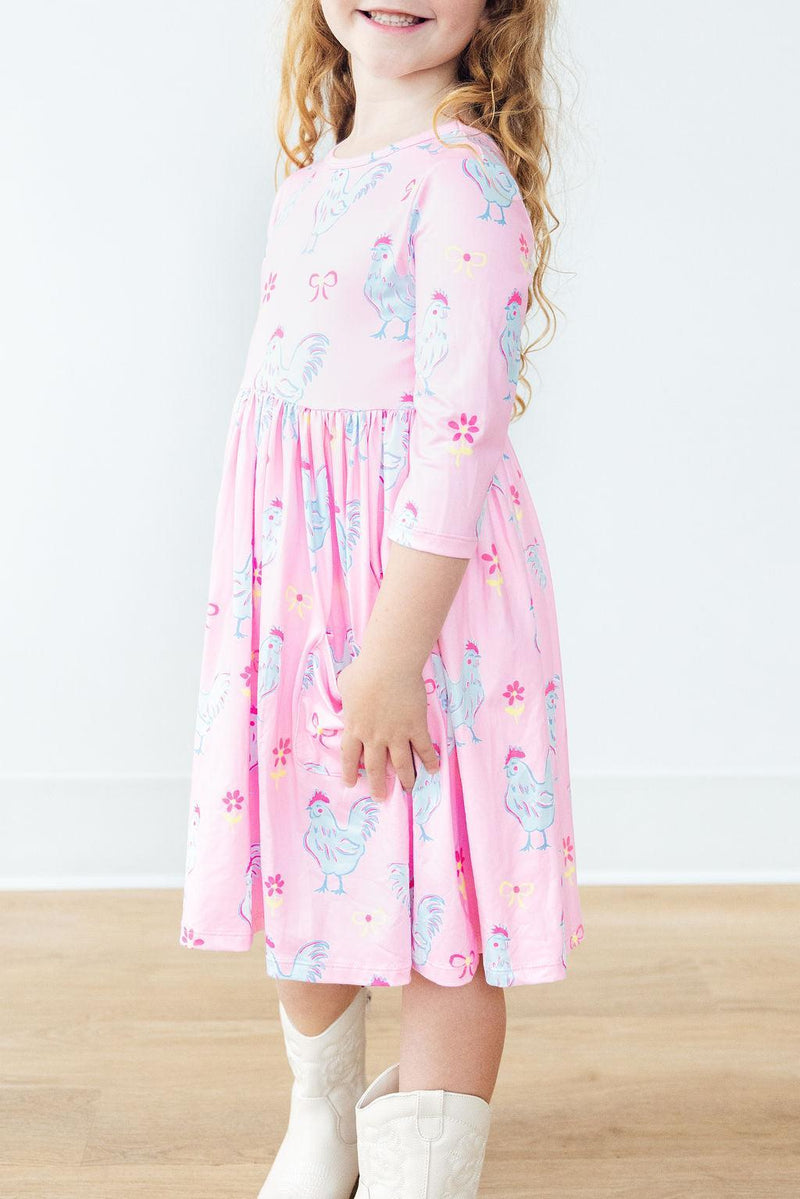 Close-up of a young girl in the Little Miss Chickie 3/4 Sleeve Pocket Twirl Dress, featuring the dress's delightful design, full-circle skirt, and relaxed fit.