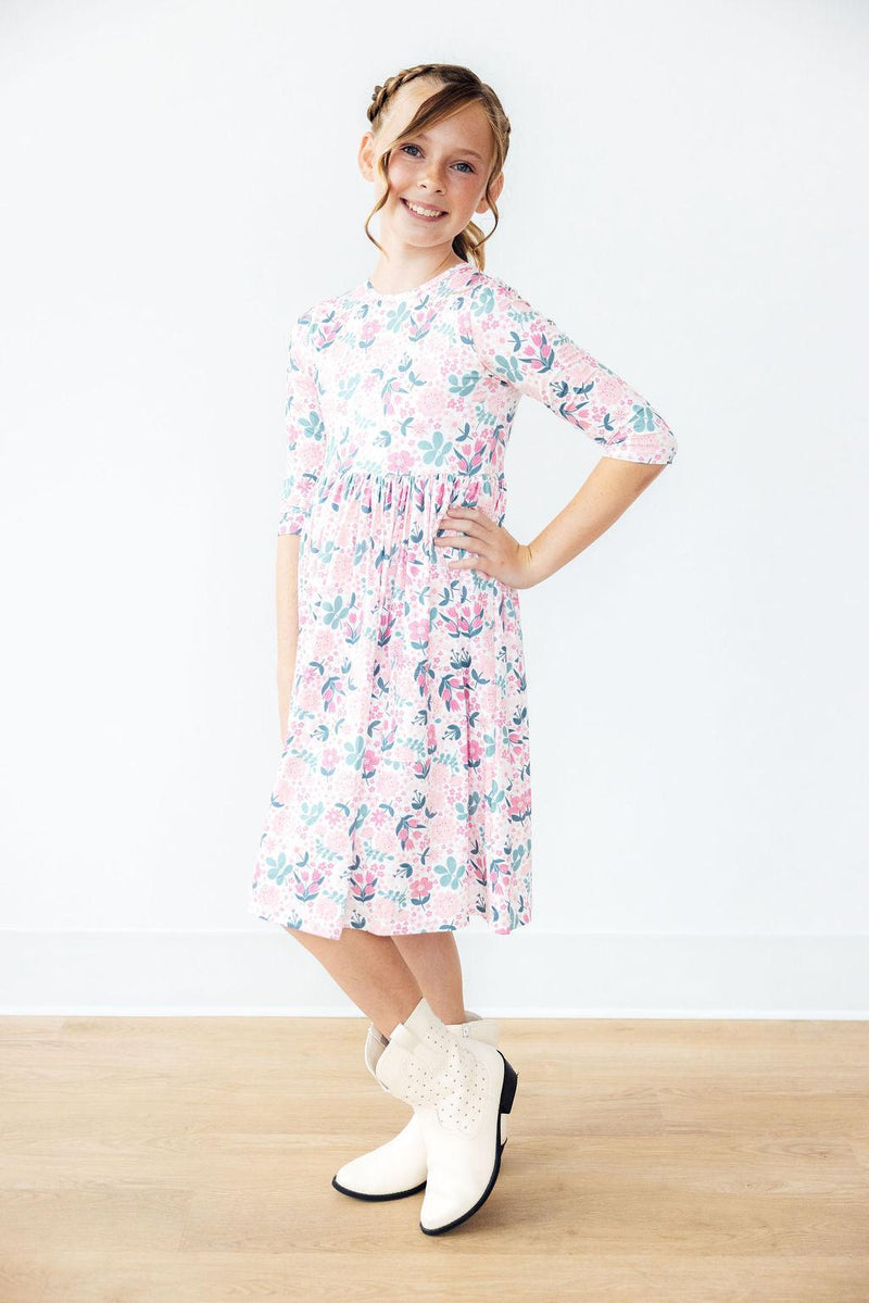 A cheerful girl posing in the Softly Blooming 3/4 Sleeve Pocket Twirl Dress by Mila & Rose®, highlighting the dress's twirl feature and stylish design paired with cute boots.