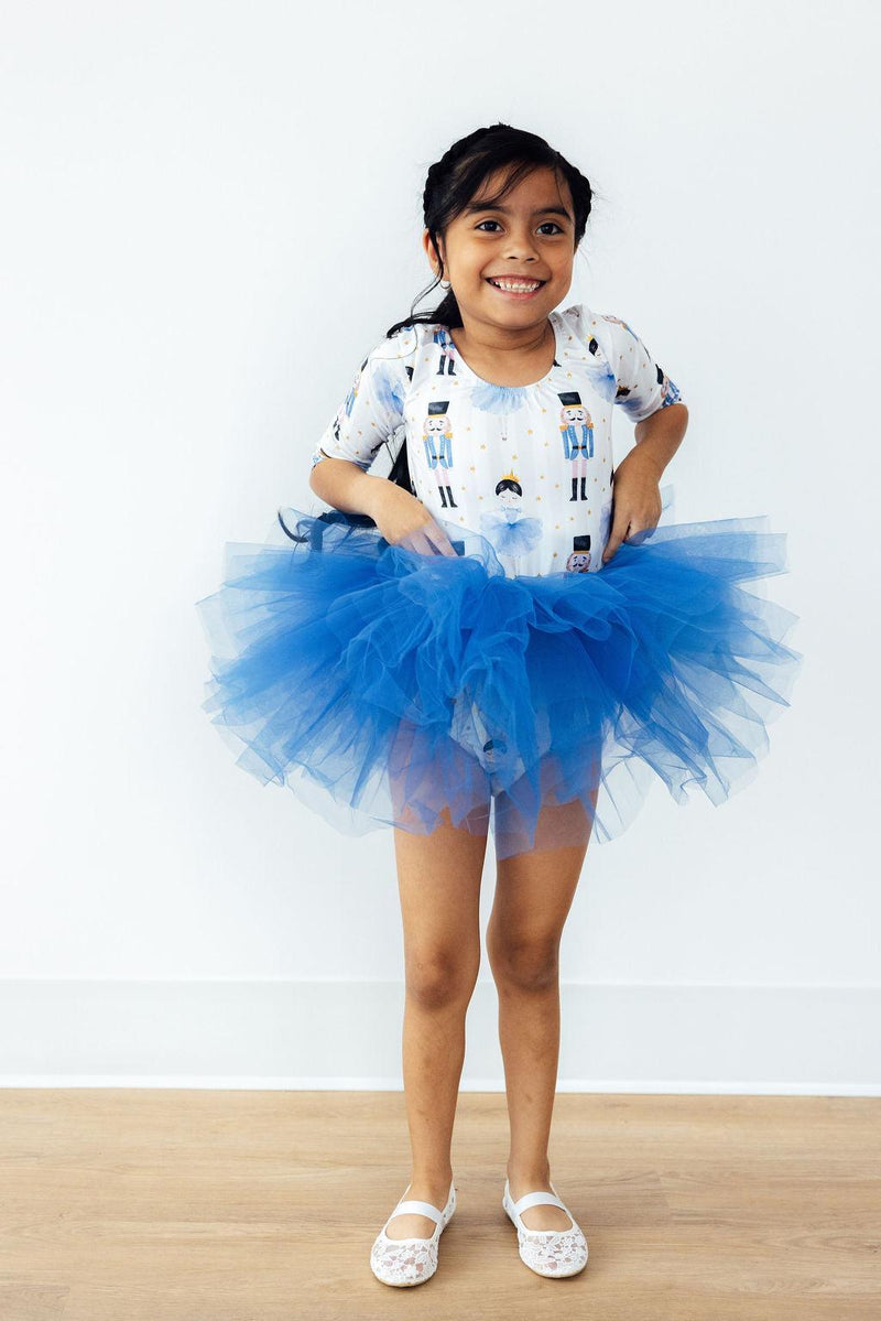 Girl holding her blue tutu wearing the Waltz of the Snowflakes 3/4 Tutu Leotard by Mila & Rose®, beaming with joy.