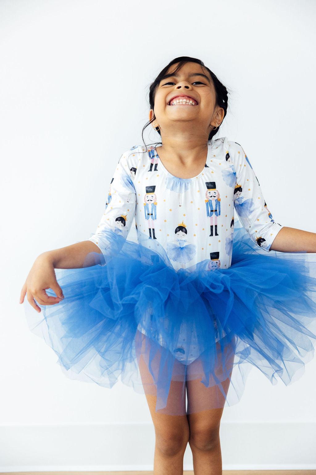 Smiling girl wearing the Waltz of the Snowflakes 3/4 Tutu Leotard by Mila & Rose®, showcasing a blue tutu and playful pose.